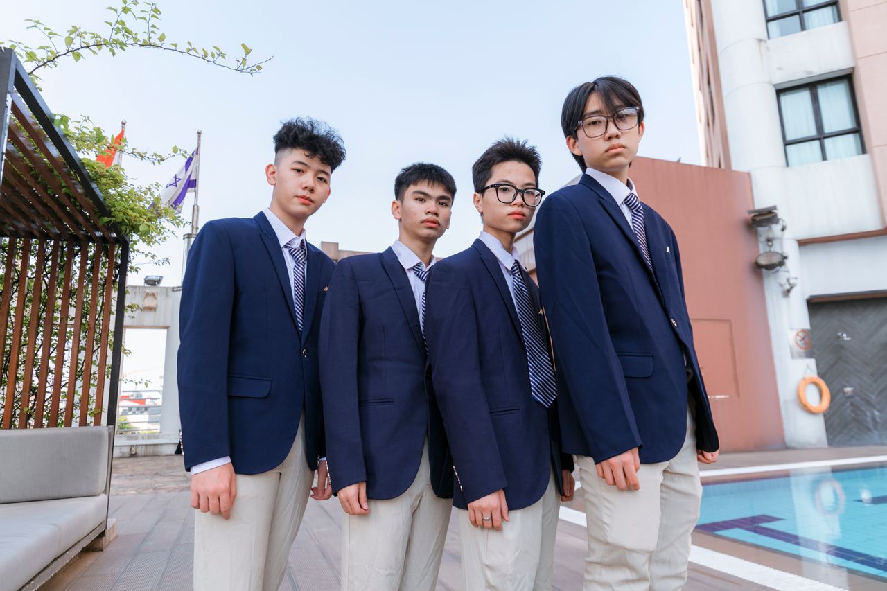 Four young students in matching uniforms stand confidently outdoors.