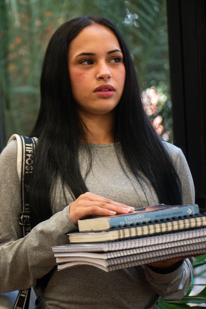 Portrait of a young woman holding books indoors, suggesting education or student life.