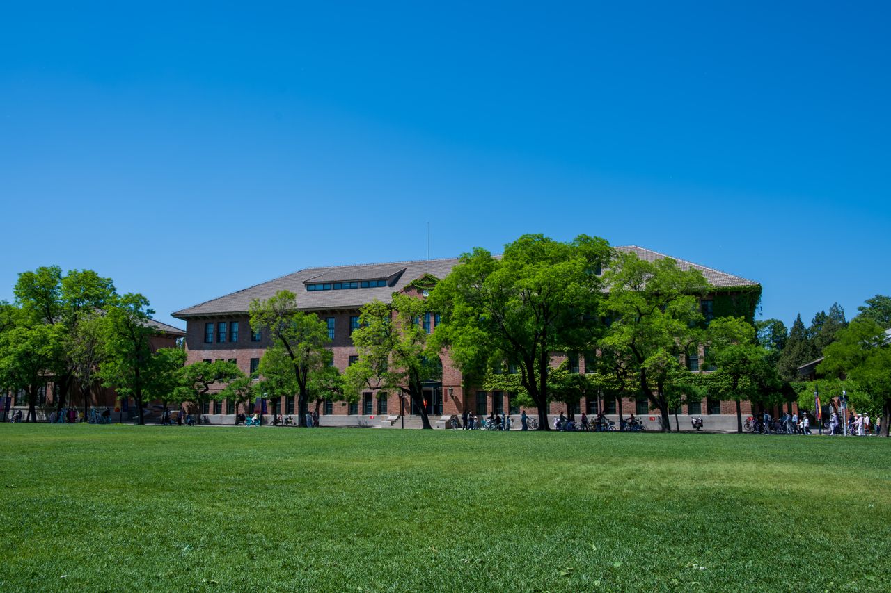 A historic brick building surrounded by lush greenery under a bright blue sky.