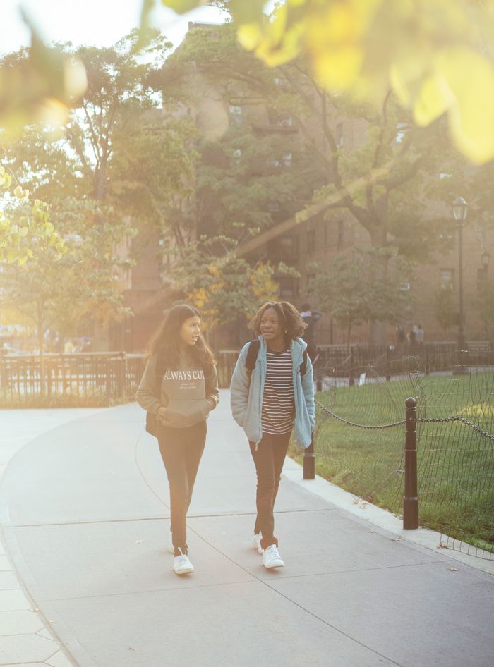 Full body of diverse classmates with backpacks strolling on pathway in park while spending time together